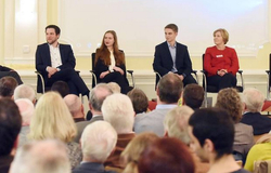 Vier Podiumsteilnehmer, zwei Männer und zwei Frauen, sitzen auf einer Bühne vor einem Publikum bei einer Veranstaltung.
