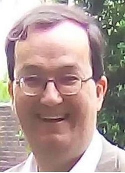 Nahaufnahme eines lächelnden ostasiatischen Mannes mit Brille und dunklem, dünner werdendem Haar vor verschwommenem Außenhintergrund.