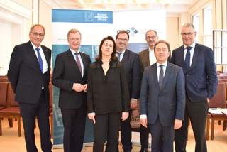 Eine Gruppe von sieben Personen, darunter eine Frau, steht vor Bannern der Konrad-Adenauer-Stiftung und der Gesellschaft für Sicherheit e.V.