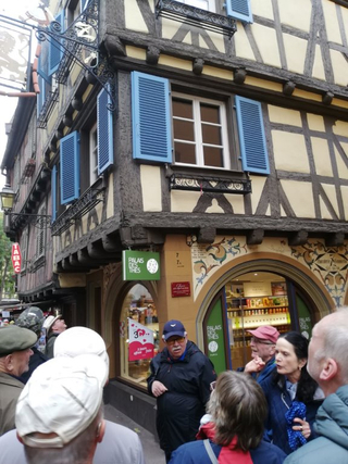 Gruppe von Menschen betrachtet ein historisches Fachwerkhaus mit blauen Fensterläden und einem "Palais des Thés" Geschäft.