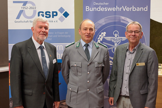 Drei Männer, einer in Uniform, vor Bannern der Gesellschaft für Sicherheitspolitik und des Deutschen BundeswehrVerbandes.