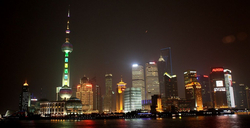Nachtansicht der beleuchteten Skyline von Shanghai mit dem Oriental Pearl Tower und vielen Wolkenkratzern, die sich im Fluss spiegeln.