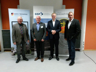 Vier Männer vor Bannern des Reservistenverbands, GSP und BundeswehrVerbands bei einer Veranstaltung.