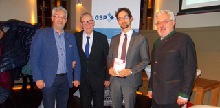 Vier Männer lächeln bei einer Veranstaltung, einer hält ein Buch namens 'Sicherheitspolitik Verstehen'.