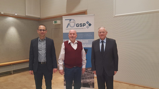 Drei Männer posieren vor einem GSP-Banner zum 70-jährigen Jubiläum der Gesellschaft für Sicherheitspolitik e.V.