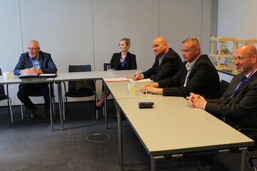 Fünf Personen in Geschäftskleidung, vier Männer und eine Frau, sitzen an einem Konferenztisch während eines Meetings.