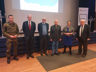 Sechs Personen, darunter ein Soldat, stehen bei einer Präsentationsveranstaltung mit einem 'Wir sind Reserve'-Banner in einer Reihe.