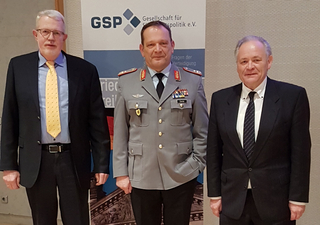 Drei Männer, einer in Militäruniform, vor einem Banner der Gesellschaft für Sicherheitspolitik (GSP).