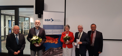 Fünf Personen, drei Männer und eine Frau, stehen vor einem GSP-Banner. Zwei halten Blumen, einer eine Medaille und Urkunde.