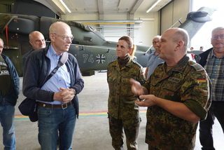 Mehrere Personen, darunter Bundeswehrsoldaten und Zivilisten, unterhalten sich in einem Hangar vor einem Militärhubschrauber.