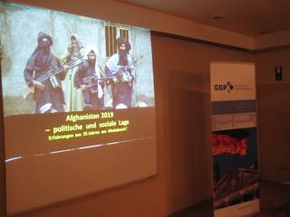 Präsentation über Afghanistan mit bewaffneten Männern und einem Banner der Gesellschaft für Sicherheitspolitik.