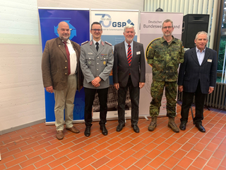 Fünf lächelnde Männer, teils in Uniform, teils zivil, posieren vor Bannern des GSP und Deutschen BundeswehrVerbandes.