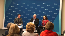 Drei Personen bei einer Podiumsdiskussion vor blauem Konrad-Adenauer-Stiftung Hintergrund. Eine Frau spricht ins Mikrofon.