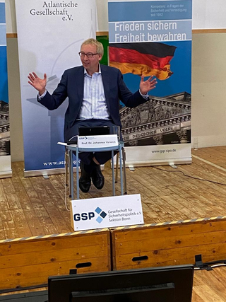 Professor Johannes Warwicks hält einen Vortrag für die GSP (Gesellschaft für Sicherheitspolitik) vor Bannern zu Frieden und Freiheit.