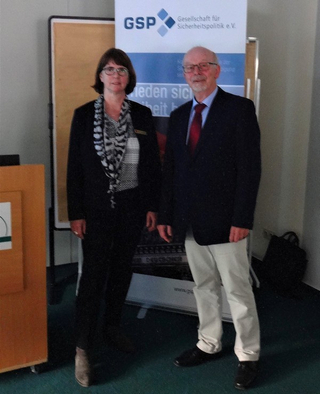 Eine Frau und ein Mann stehen lächelnd vor einem Banner der Gesellschaft für Sicherheitspolitik (GSP).