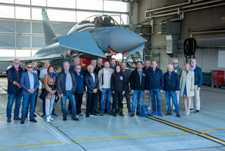 Eine Gruppe Erwachsener posiert vor einem Eurofighter Typhoon Militärjet in einem hellen Flugzeughangar.