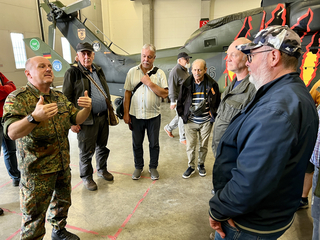 Soldat in Bundeswehr-Uniform erklärt Zivilisten Militärhubschrauber in einer Halle, mit ISAF- und UN-Markierungen.