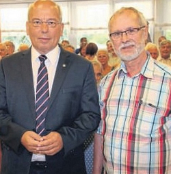 Zwei Männer stehen nebeneinander: Einer im Anzug, der andere im karierten Hemd, mit Brille und Bart.