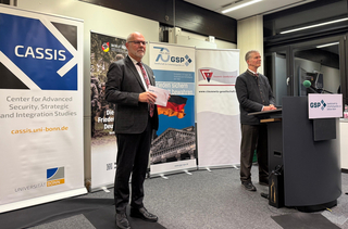 Zwei Männer bei einem Vortrag. Im Hintergrund Banner von CASSIS, GSP und Clausewitz-Gesellschaft zur Sicherheitspolitik.