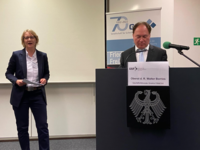 Frau präsentiert, Mann (Walter Borries) sitzt an einem GSP-Podium mit Bundesadler-Emblem, vermutlich bei einer Konferenz.