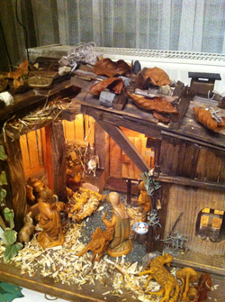 Eine detaillierte, beleuchtete Weihnachtskrippe mit Holzstall, Maria, Josef, Jesuskind, Hirten und Tieren.