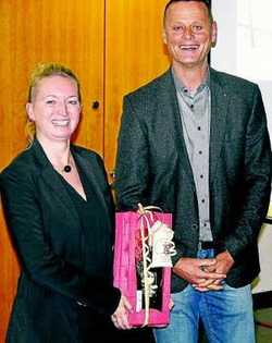 Lächelnde Frau mit pinker Geschenktüte neben lächelndem Mann bei einer Übergabe.