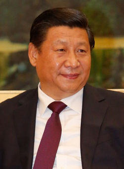 Nahaufnahme des chinesischen Präsidenten Xi Jinping, leicht lächelnd, in dunklem Anzug und bordeauxroter Krawatte.