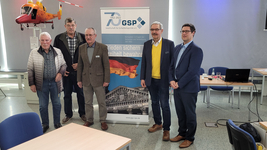 Fünf Männer bei einer GSP-Veranstaltung mit einem 70-Jahre-Banner und einem Hubschraubermodell im Hintergrund.