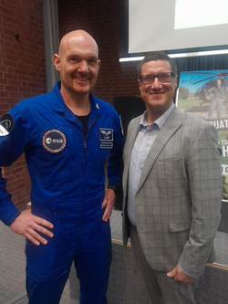 ESA-Astronaut Alexander Gerst im blauen Fluganzug mit einem lächelnden Mann im grauen Anzug posieren.