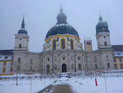 Verschneites Barockkloster mit großer Kuppel und zwei Glockentürmen, an einem nebligen Wintertag zu sehen.