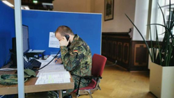 Ein Mann in Bundeswehr-Uniform telefoniert und schreibt an einem Schreibtisch in einem Büro.