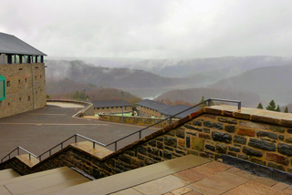 Steingebäude und Treppen mit Blick auf ein nebliges, bewaldetes Tal mit See an einem bewölkten Tag.
