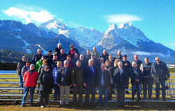 Eine große Gruppe Menschen steht bei strahlendem Sonnenschein vor majestätischen, schneebedeckten Bergen.