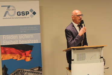 Ein Mann spricht am Rednerpult. Dahinter zeigt ein GSP 70-Jahre-Banner die deutsche Flagge und Sicherheitsslogans.