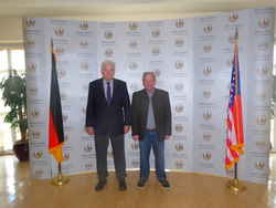 Zwei Männer stehen zwischen deutscher und US-Flagge vor einem Logo-Hintergrund des George C. Marshall Centers.