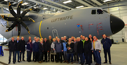 Eine Gruppe Erwachsener posiert vor einem großen grauen Transportflugzeug A400M der deutschen Luftwaffe im Hangar.