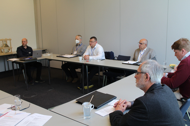 Eine Gruppe von Fachleuten bei einer Besprechung an Tischen in einem hellen Konferenzraum, einige machen sich Notizen.