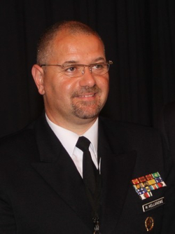 Lächelnder Mann in Uniform mit Brille, Ziegenbart und militärischen Bändern, Namensschild 'M. HELLGREWE'.