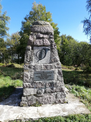 Steinernes Denkmal mit Jagdhornrelief und Plakette für den Vorposten des 28. BCA vom Jan. 1915, umgeben von Bäumen.