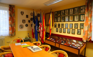 Ein Zimmer mit gelben Wänden, geschmückt mit Flaggen, gerahmten Porträts und einer Vitrine voller militärhistorischer Exponate.