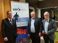 Drei Männer stehen vor einem Banner der Gesellschaft für Sicherheitspolitik (GSP), Sektion Lippstadt.