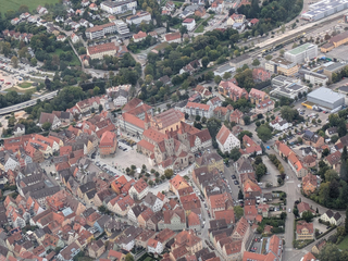 Luftaufnahme einer historischen europäischen Stadt mit einem markanten Kirchenkomplex mit roten Dächern inmitten traditioneller Gebäude.