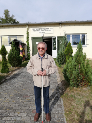 Mann mit Sonnenbrille und Blindenstock vor dem Militärhistorischen und Technischen Museum Eggesin.