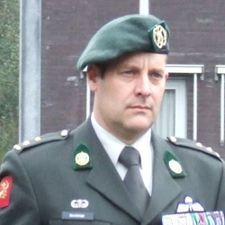 Porträt eines Mannes in dunkler grüner Militäruniform, mit Barett, Krawatte und mehreren Medaillenbändern.