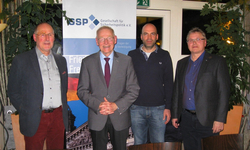 Vier Männer lächeln und posieren für ein Gruppenfoto vor einem Banner der 'Gesellschaft für Sicherheitspolitik e.V.' (GSP).
