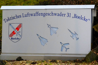 Schild des Taktischen Luftwaffengeschwaders 31 „Boelcke“ mit Wappen und vier Kampfjet-Silhouetten.