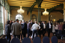 Menschen unterhalten sich in einem großen, eleganten Saal mit grünen Bögen und Kronleuchtern bei einer Veranstaltung.