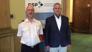 Zwei Männer stehen vor einem Banner der Gesellschaft für Sicherheitspolitik (GSP). Einer trägt eine Uniform, der andere einen Blazer.