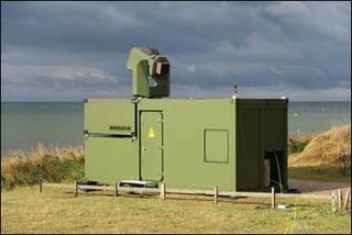 MBDA Militärcontainer mit Lasersystem-Turm an einer grasbewachsenen Küste am Meer.