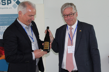 Ein Mann überreicht einem anderen eine Flasche Wein mit Geburtstagsgrüßen bei einer GSP-Veranstaltung.